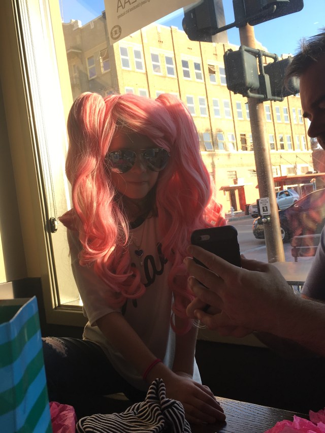 C.J. at Starbucks after brunch, checking out pictures on Uncle Michael's phone and wearing the wig his best friends gave him.